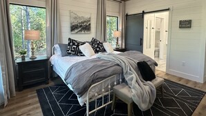 Una camera da letto con un letto, comodini, una finestra con tende, un quadro e un cartello appeso al muro.