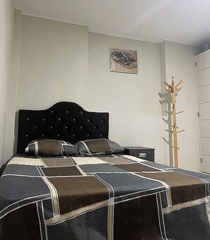 Cozy retreat with a neatly made bed, tufted headboard, and a wooden coat rack.