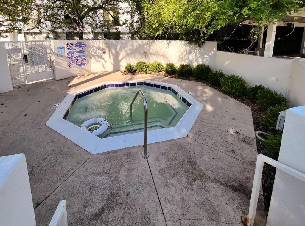 A swimming pool with a safety sign, surrounded by a concrete deck and a white wall.