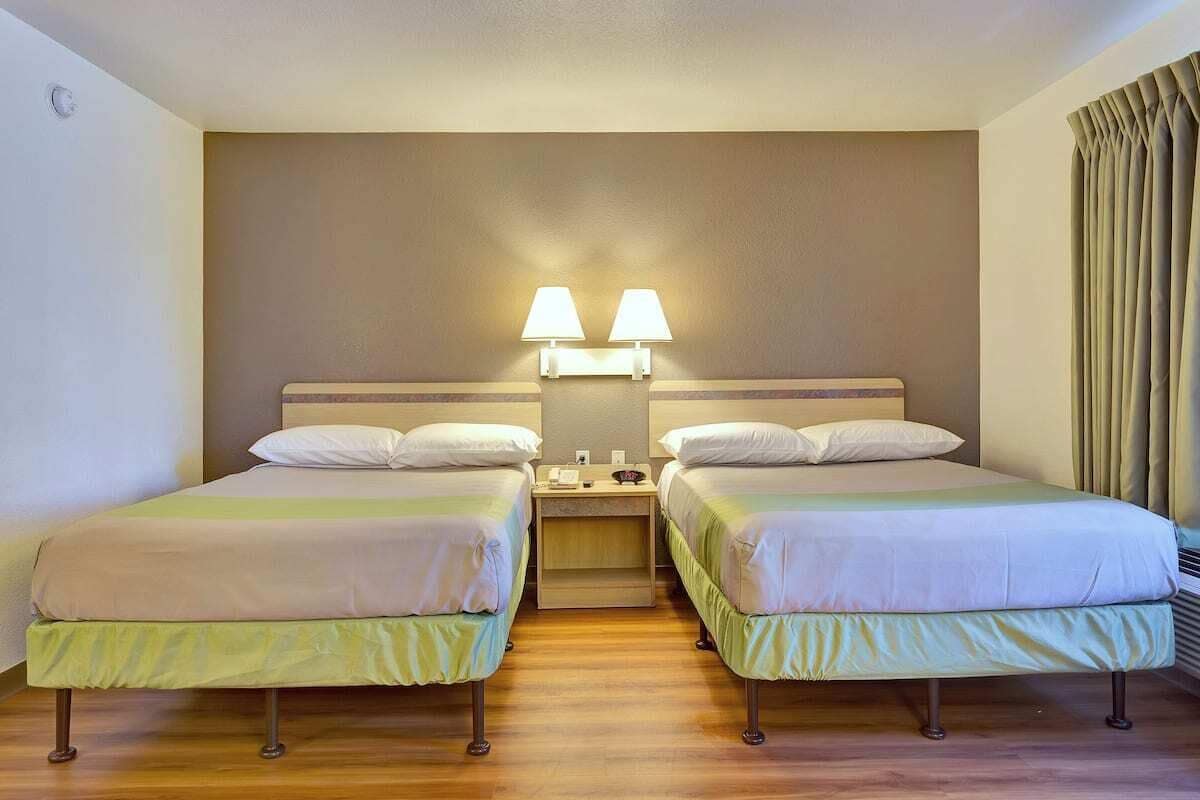 A hotel room with two beds, a nightstand, and a wall-mounted lamp.