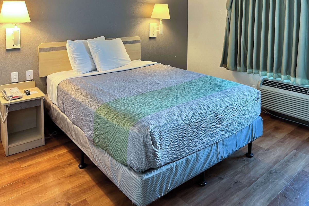 A neatly made bed with a patterned bedspread, two bedside lamps, a bedside phone, and a power outlet on the nightstand.