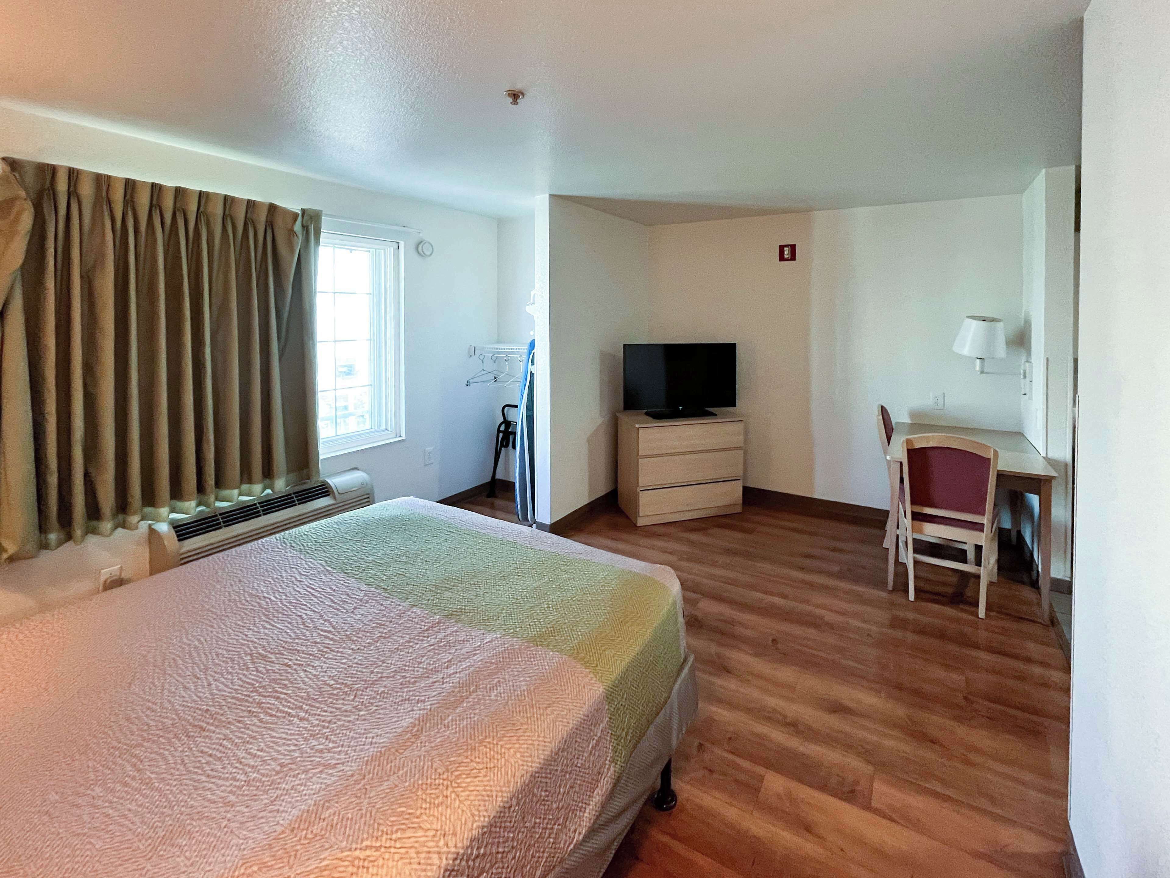 A hotel room with a bed, a desk, a chair, a television, and a window with curtains.