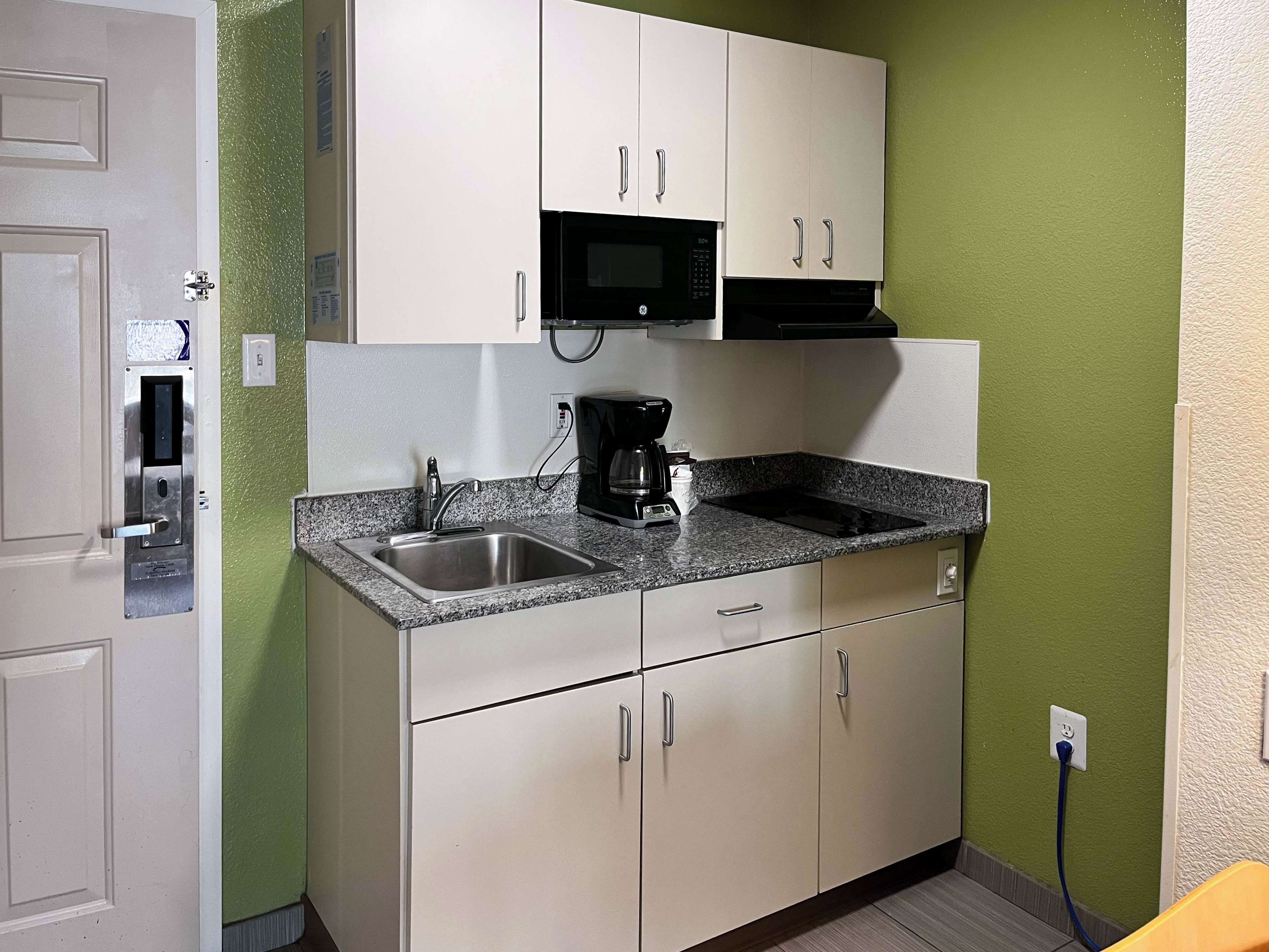 A compact kitchen with a granite countertop, stainless steel sink, and white cabinets.