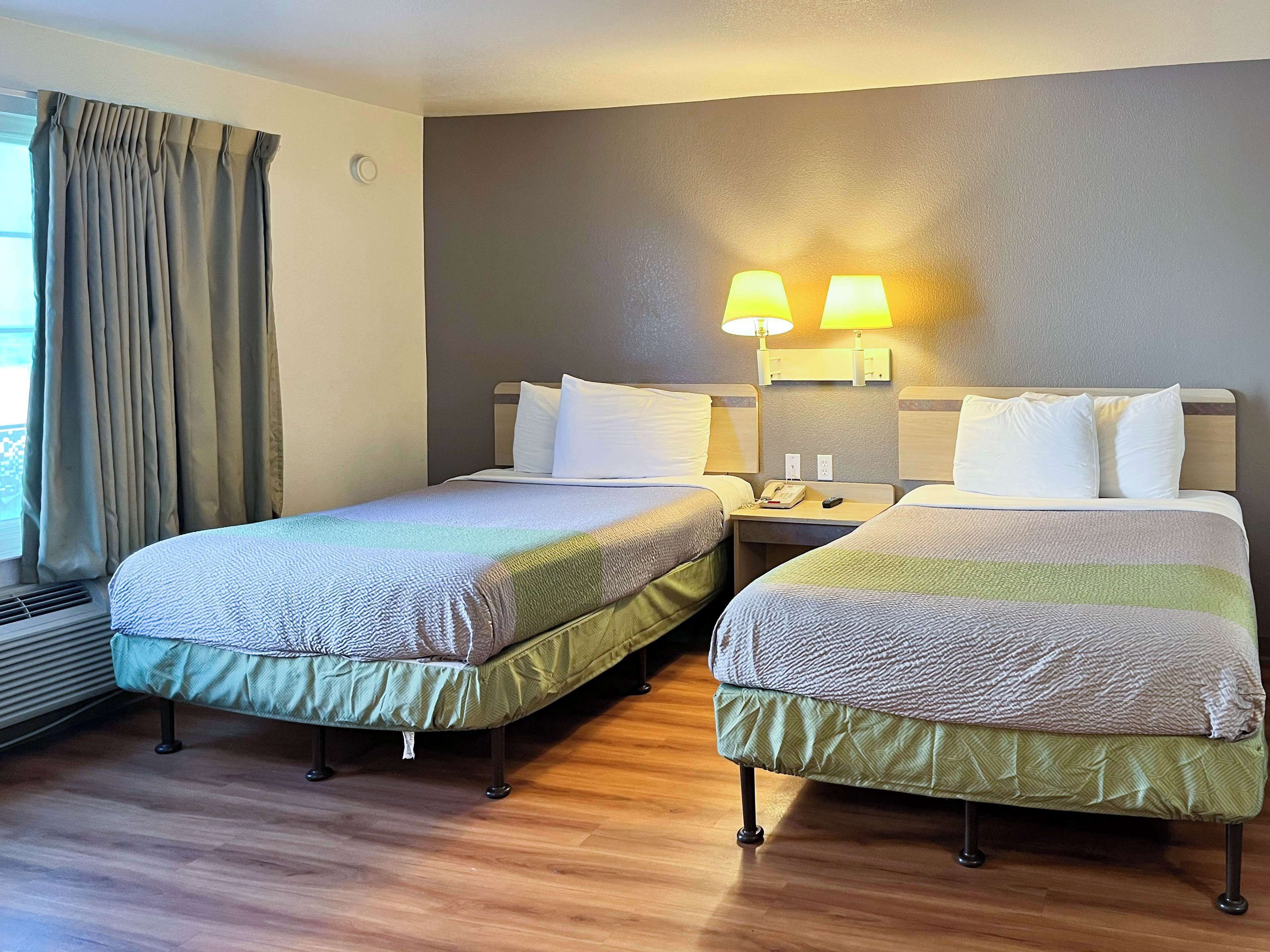 A hotel room with two beds, a nightstand with a lamp, and a window with curtains.