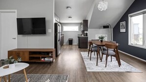 Una sala moderna con televisor de pantalla plana, mueble de entretenimiento de madera y una zona de comedor con mesa y sillas.