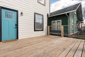 A wooden deck with a blue door, a window, and a green building in the background.
