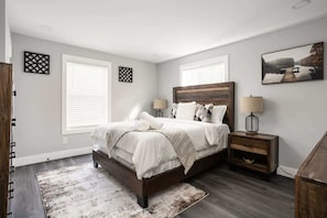 A bedroom with a bed, two bedside tables, a rug, and a painting on the wall.