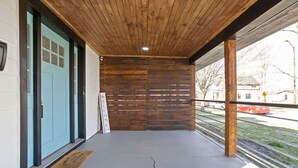 A covered porch with a wooden ceiling, a blue door, and a view of the street. - Heart of Indy | Sleeps 6 | Modern Home (Indianapolis)