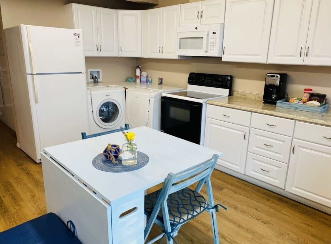 A compact kitchen with white cabinets, a microwave, a stove, a washing machine, and a coffee maker.
