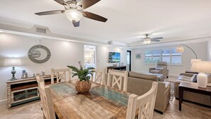 A spacious living room with a wooden dining table, beige sofas, and ceiling fans. - Steps to Siesta Key Beach! We offer 3-night rentals! Beach gear included! (Sarasota)
