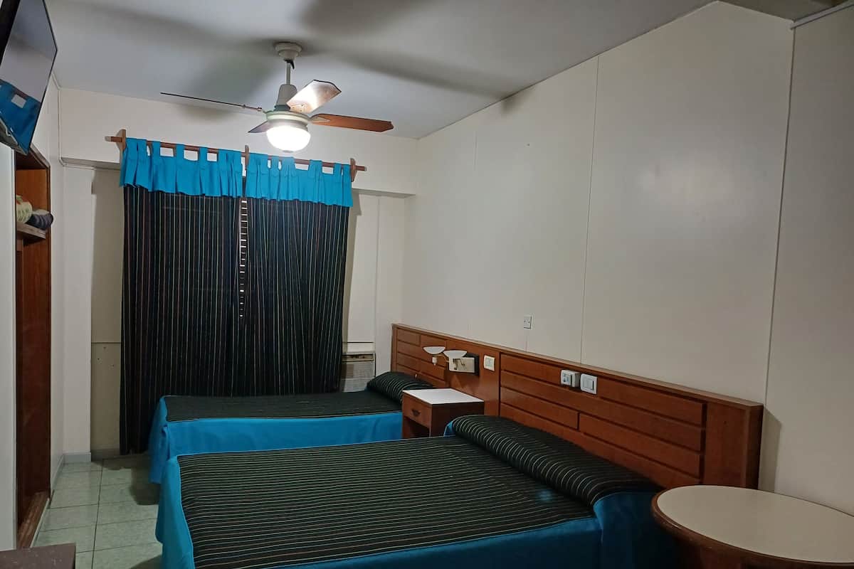 Una habitación pequeña y acogedora con dos camas individuales, cabecero de madera, una mesita y un ventilador de techo.