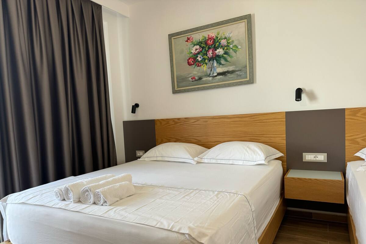 A hotel room with a large bed, two bedside tables, a painting on the wall, and a window with curtains.