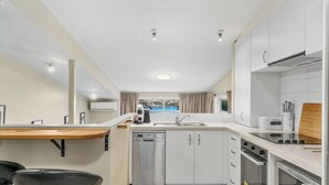 Cocina compacta con armarios blancos, lavavajillas, estufa y cafetera.