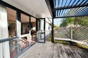 Une terrasse en bois avec une porte vitrée donnant sur une pièce comprenant un lit et une chaise.