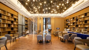 Una biblioteca moderna con estanterías de madera, asientos cómodos y un techo con numerosas luces.