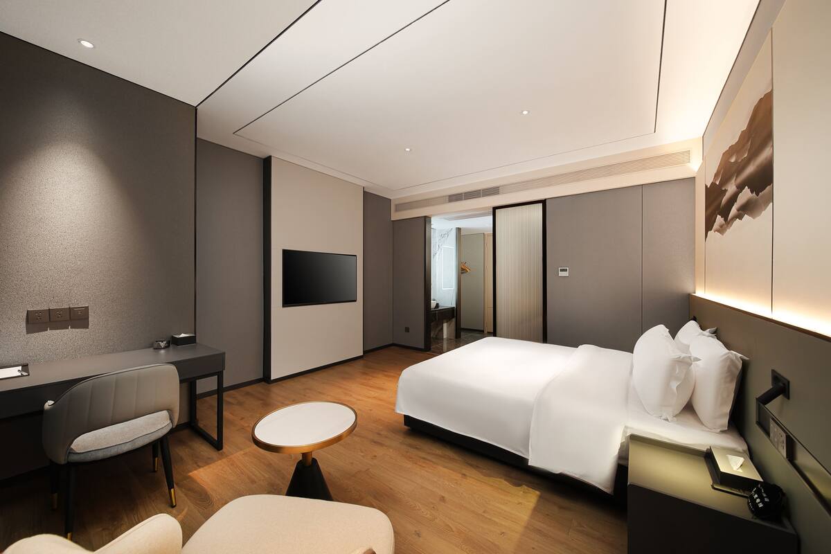 Quarto de hotel moderno com cama, escrivaninha, cadeira e uma pequena mesa redonda.
