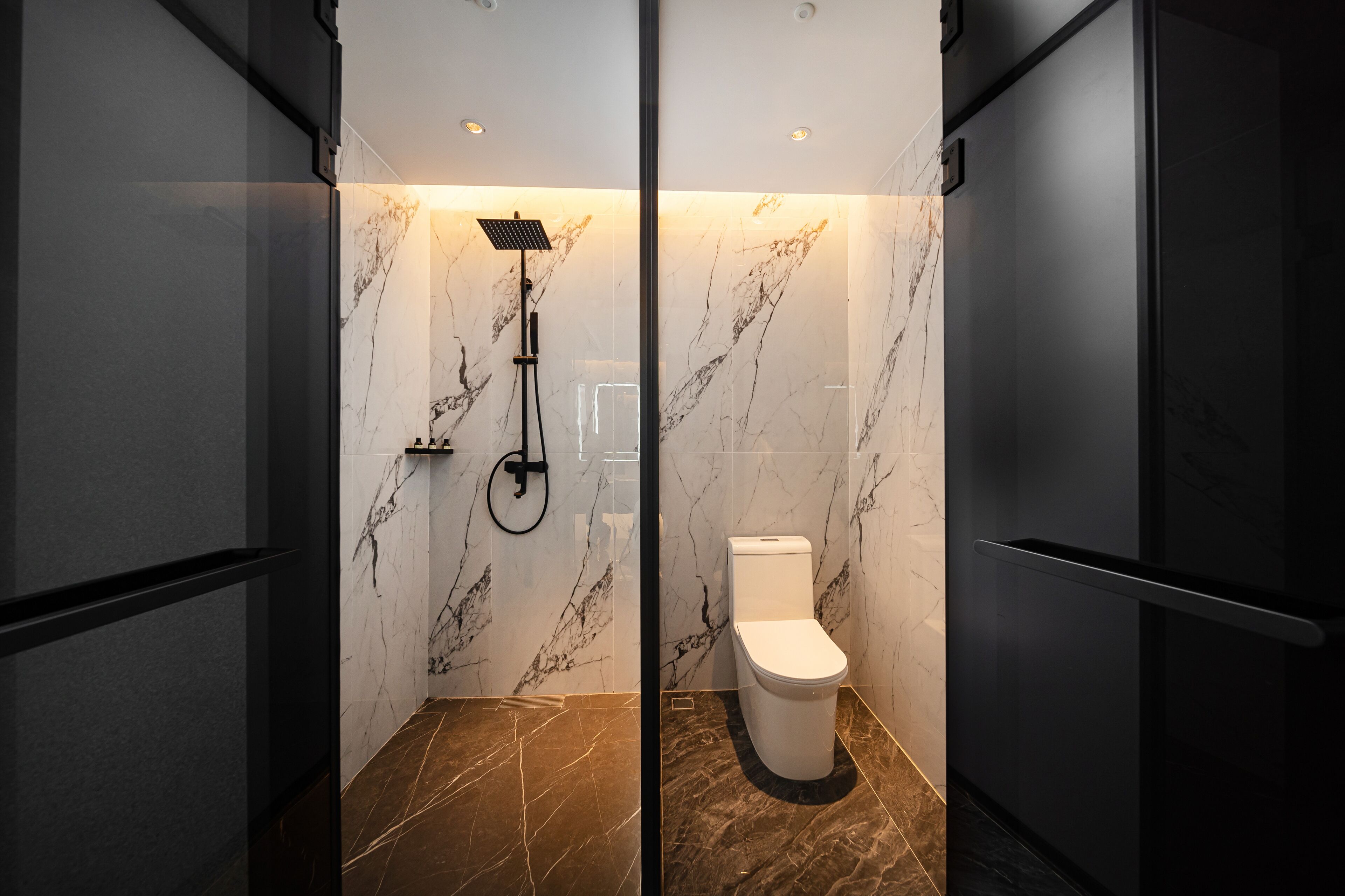 A modern bathroom with a shower, toilet, and marble walls.