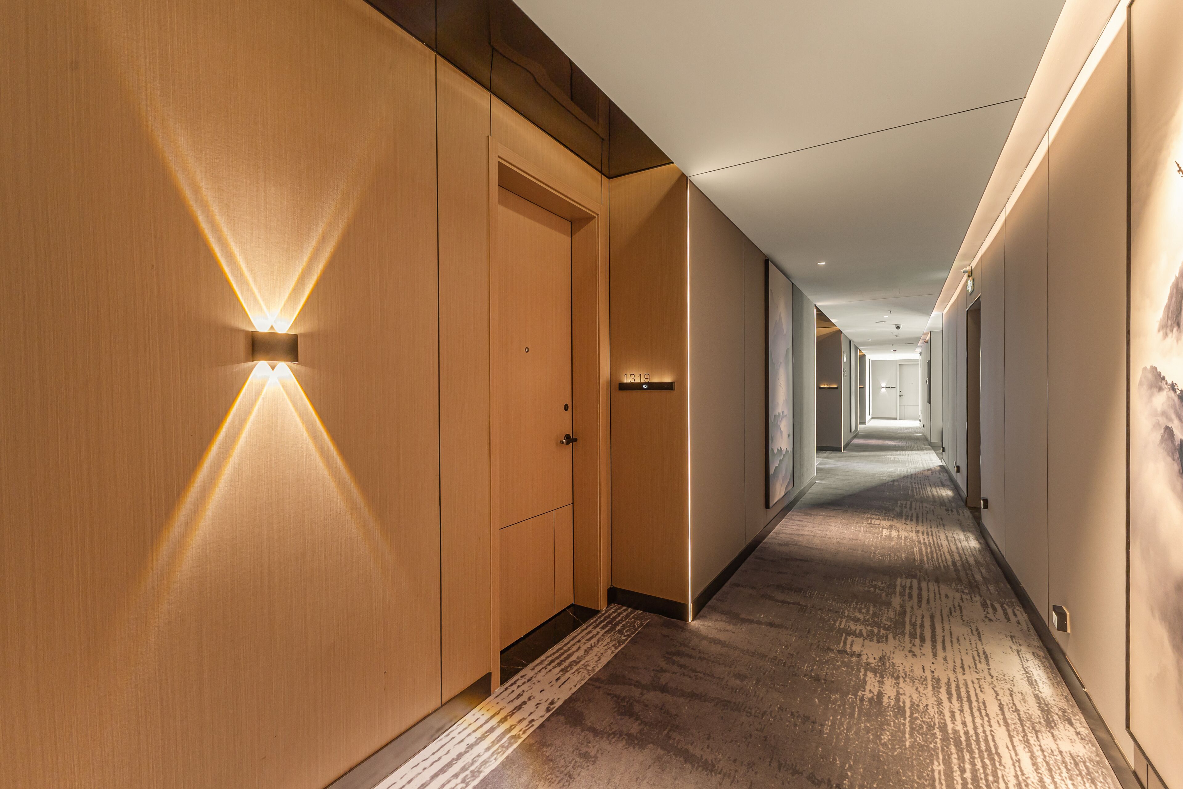 Un pasillo moderno de hotel con paneles de madera, iluminación empotrada y suelo alfombrado.