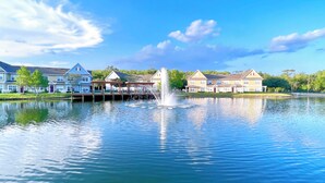 A lake with a fountain, surrounded by residential buildings with a dock and a white picket fence.