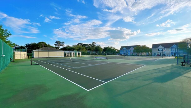 An outdoor tennis court with a net, green surface, and surrounding fencing.