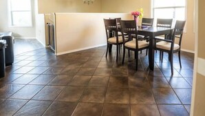 A dining area with a dark tiled floor, a central table with chairs, and a chandelier. - Beautiful home in quiet neighbourhood, sleeps 10! (Grande Prairie)