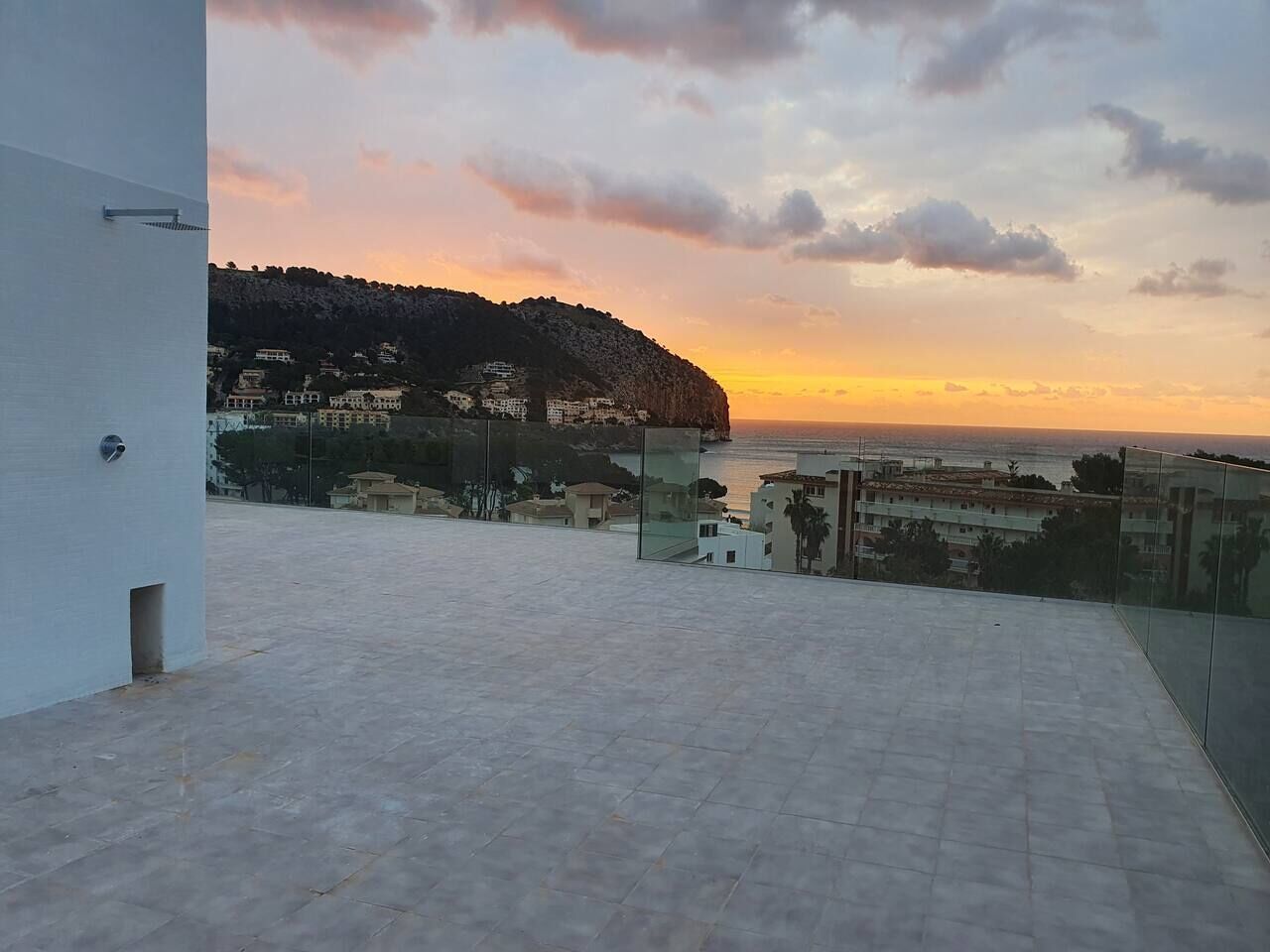 A rooftop terrace with a view of a coastal town at sunset.