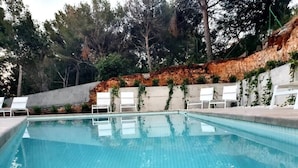 A swimming pool with clear blue water, surrounded by white lounge chairs and a concrete wall with greenery. - Sea apartment 1A with pool, 2 min. canyamel beach (Capdepera)
