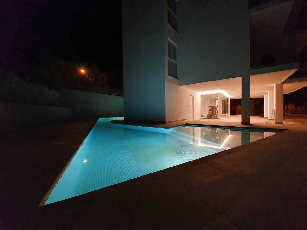 Ein modernes Haus mit Swimmingpool bei Nacht, beleuchtet durch Poollichter.