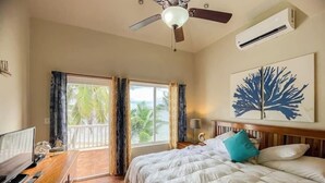 Une chambre d’hôtel comprenant un lit, un bureau avec un ordinateur, un ventilateur de plafond, un climatiseur et une fenêtre avec des rideaux.