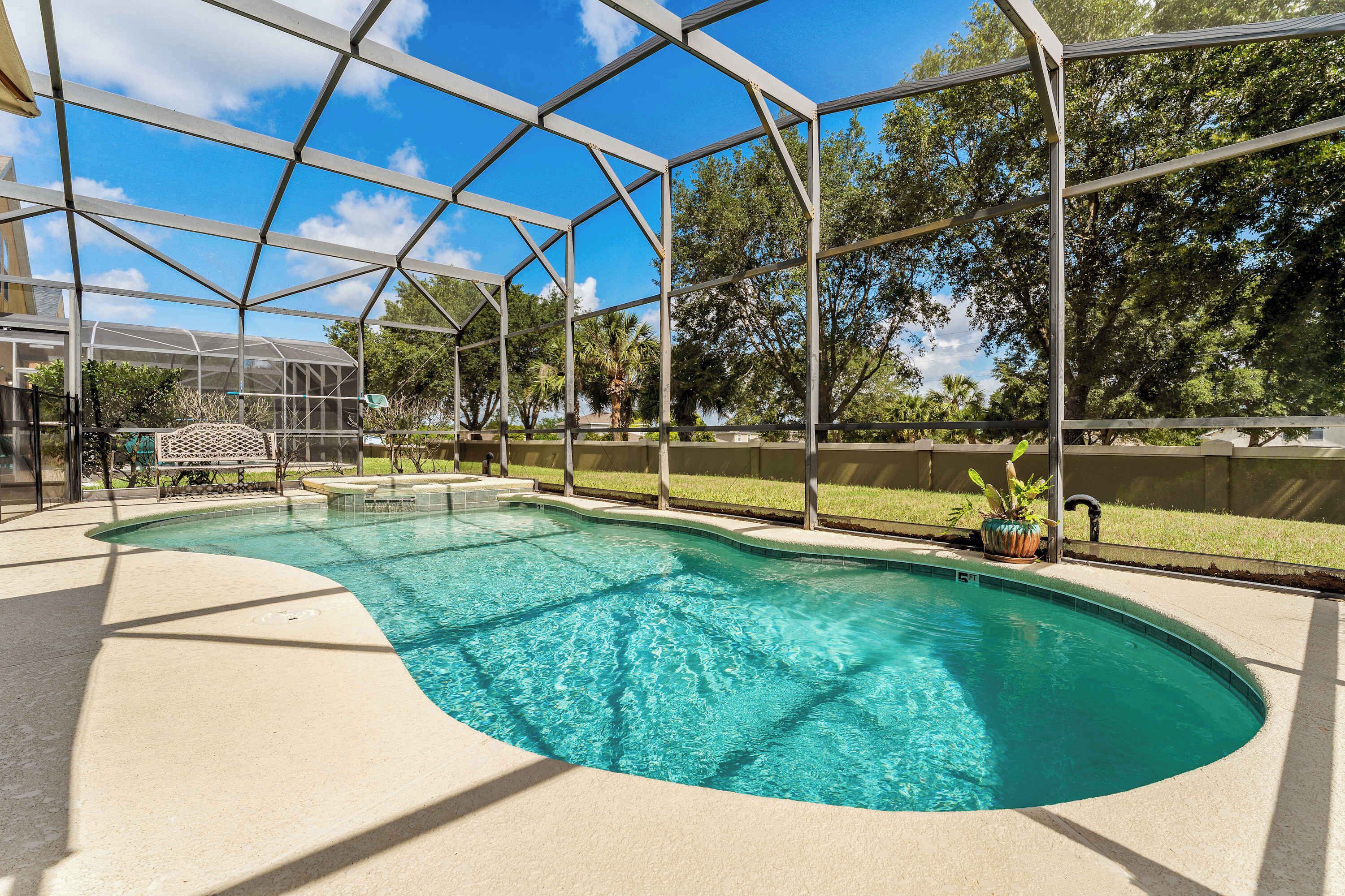 Une piscine à l’eau d’un bleu limpide, entourée d’une zone abritée dotée d’une structure métallique et de panneaux de verre.