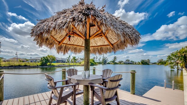 Eine Holzterrasse mit einem Strohdach, einem Tisch und Stühlen mit Blick auf einen ruhigen See.