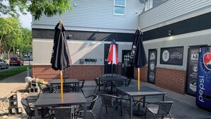 An outdoor seating area with tables and chairs, a brick wall, and a Pepsi vending machine.