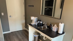 A modern kitchen with a stainless steel sink, a coffee maker, a kettle, and a trash can.