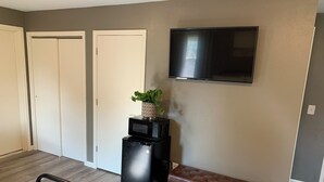 A compact living space with a kitchenette, a flat-screen TV mounted on the wall, a bench, and a door.
