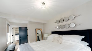 A bedroom with a large bed, a bench, a wardrobe, and a mirror wall.