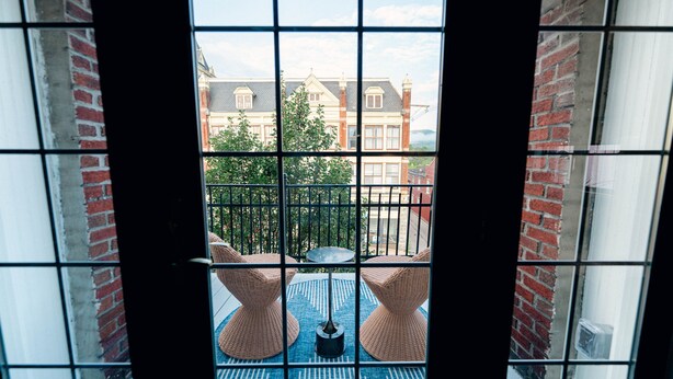 A balcony with wicker chairs and a table, a view of a building with a brick facade, and a clear sky.