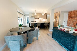 Una cocina moderna con una isla central, taburetes de bar, iluminación colgante y una pared de ladrillo decorativa.