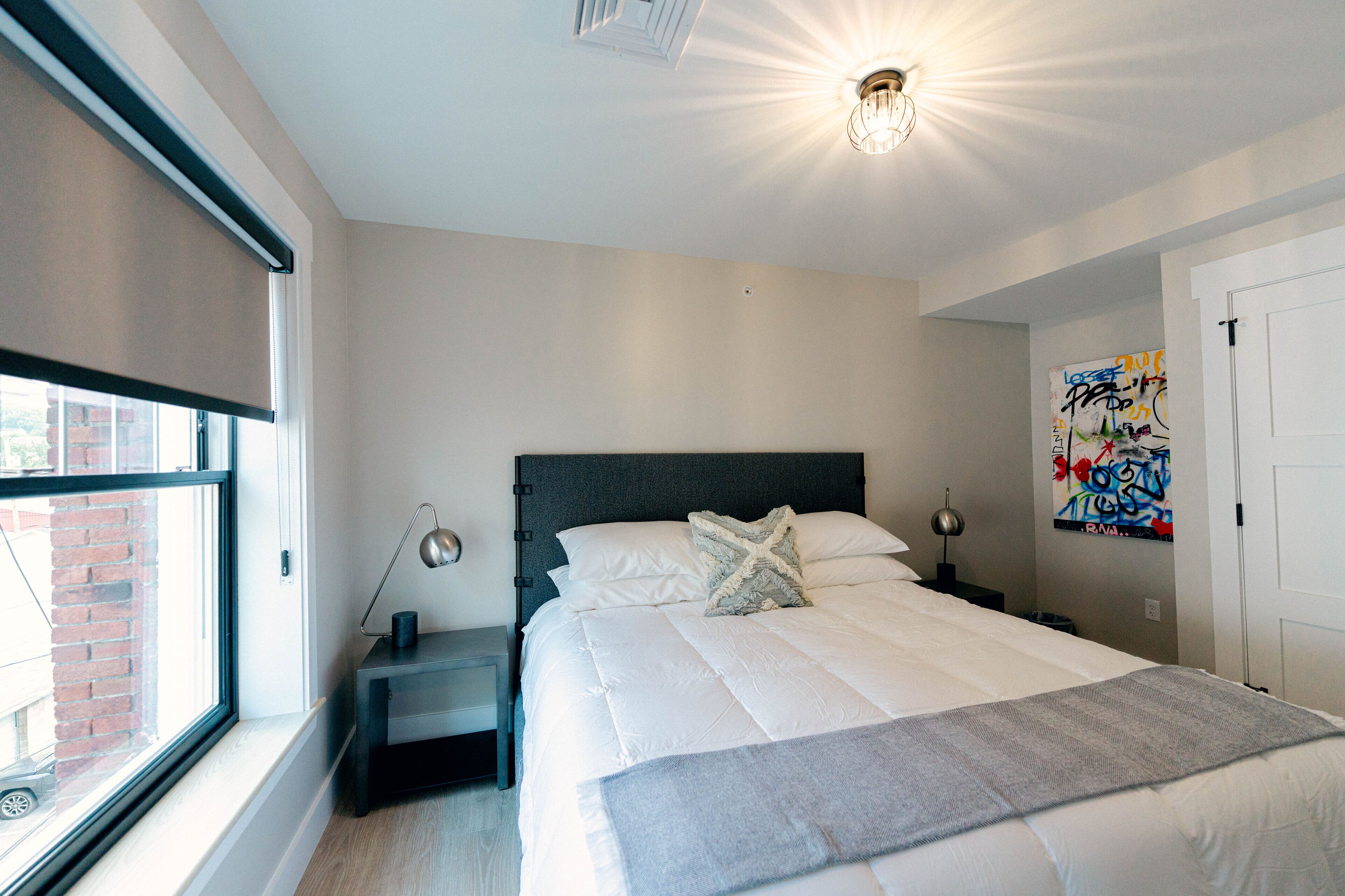 Un dormitorio con cama, mesitas de noche, una ventana y una pared con grafitis.