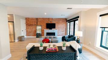 A modern living room with a brick wall, a fireplace, a flat-screen TV, and a sofa.