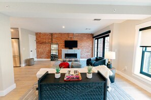 Una sala de estar moderna con una pared de ladrillo, una chimenea, un televisor de pantalla plana y un sofá.