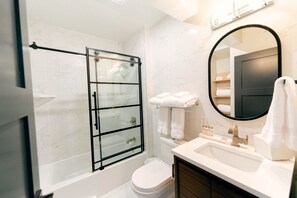 Un baño moderno con ducha de vidrio, inodoro blanco y tocador con lavamanos y espejo.