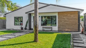 Uma casa moderna de dois andares com fachada branca, porta de garagem de madeira e gramado bem cuidado.