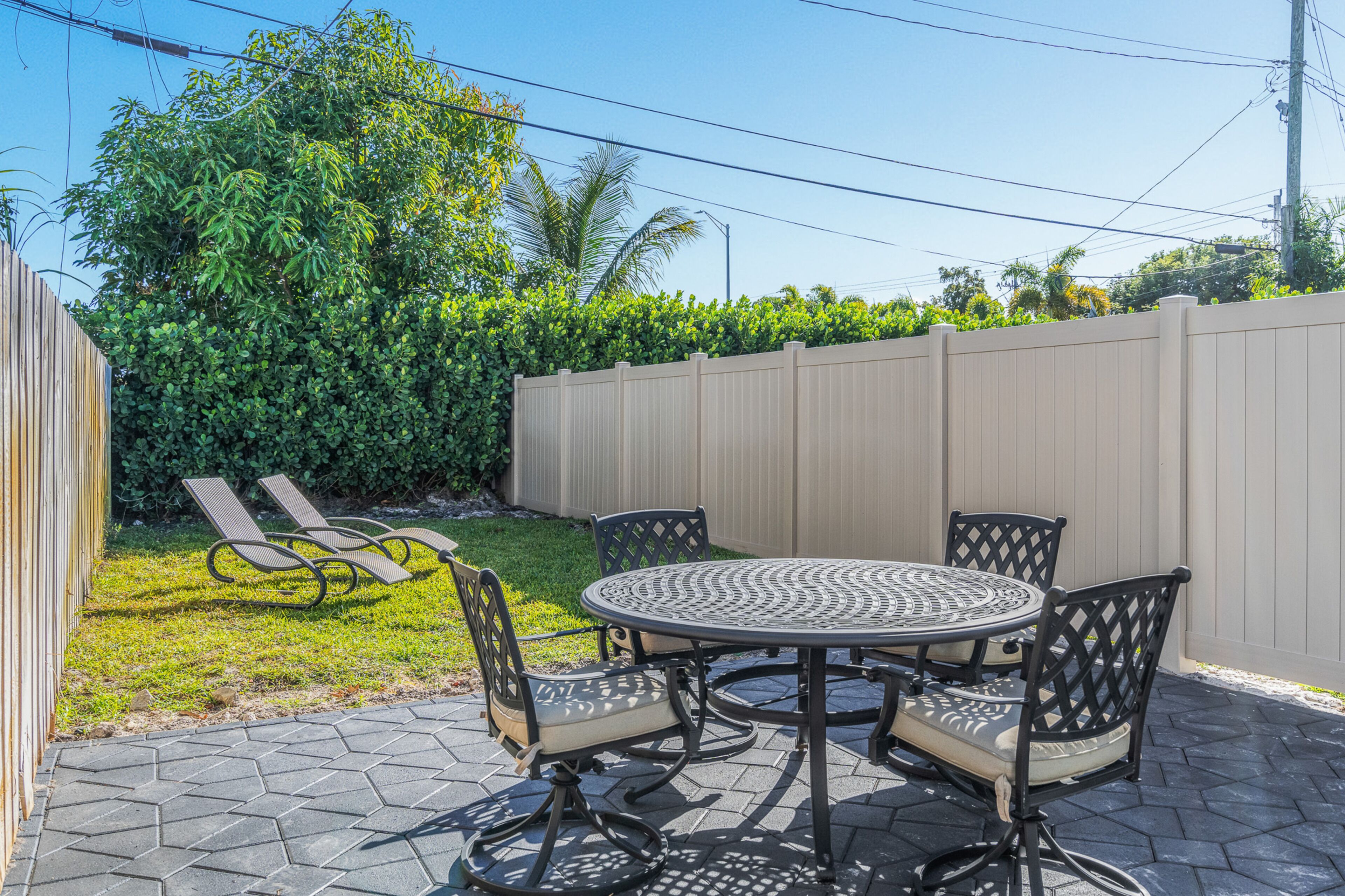An outdoor patio with a round table and four chairs, surrounded by a wooden fence and lush greenery.