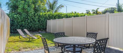 An outdoor patio with a round table and four chairs, surrounded by a wooden fence and lush greenery.