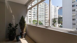 Une pièce dotée d’une grande fenêtre, de plantes en pot et offrant une vue sur des immeubles de grande hauteur.