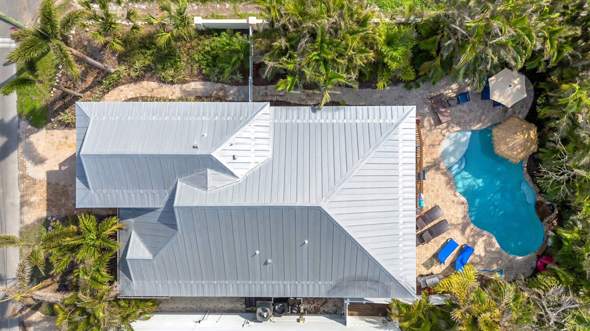An aerial view of a house with a sloped roof, a swimming pool, and surrounding tropical vegetation.