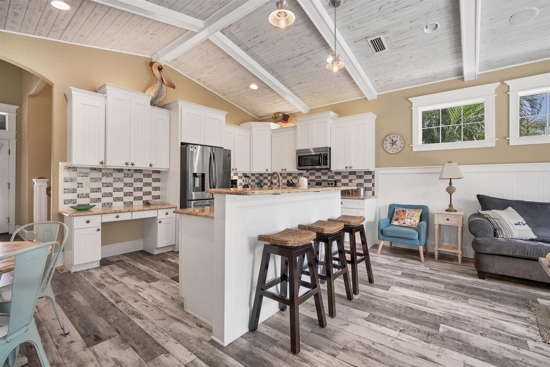 A spacious kitchen with white cabinets, a central island with stools, a microwave, and a refrigerator.