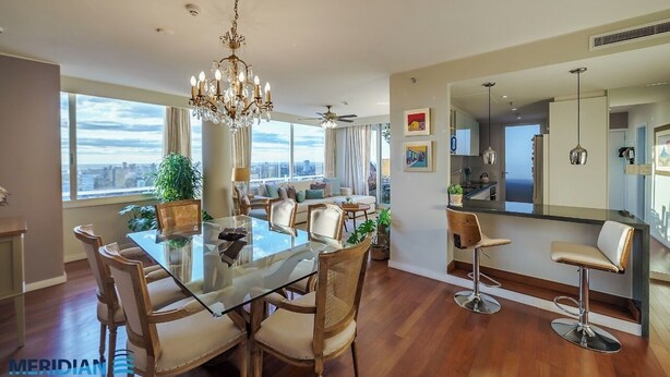 Uma sala de jantar moderna com mesa e cadeiras de vidro, um lustre e vista para a cidade.