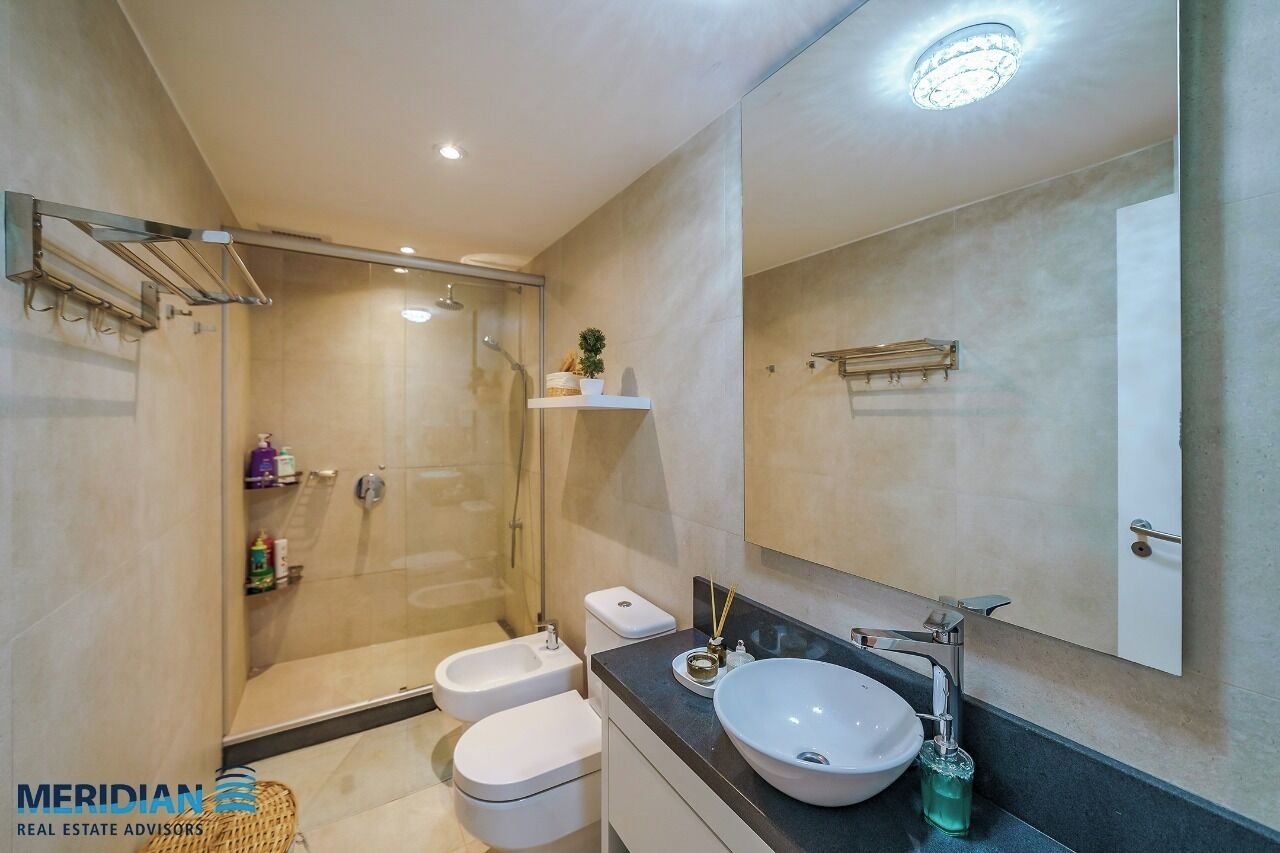 A modern bathroom with a glass-enclosed shower, a white toilet, a sink with a large basin, and a mirror above the sink.