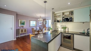 Cozinha moderna com ilha central, eletrodomésticos de aço inoxidável e área de refeições com lustre.